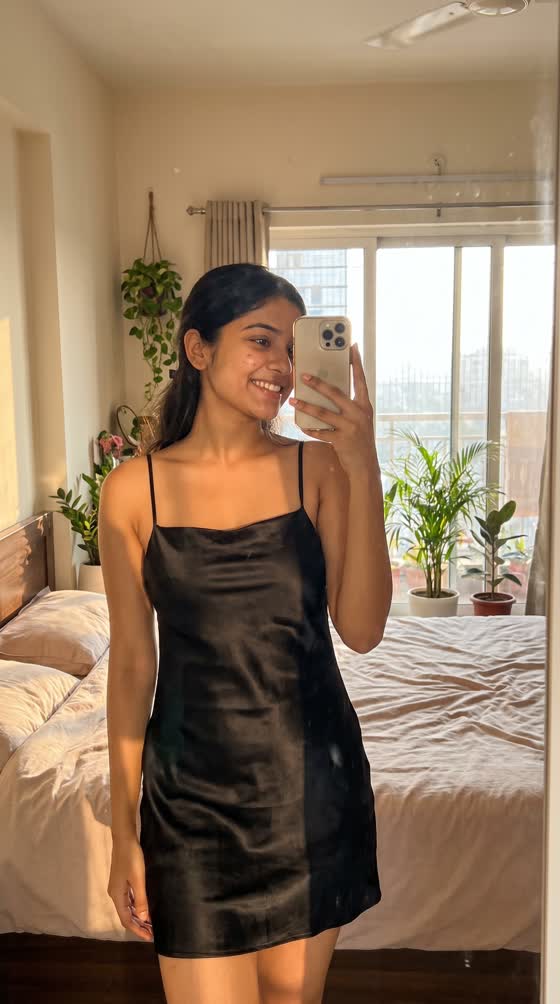 A customer in a black satin slip dress taking a mirror selfie.
